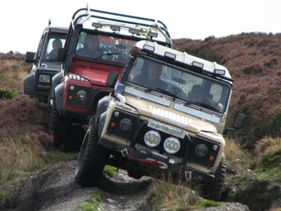 Three Land Rovers driving down a green lane.