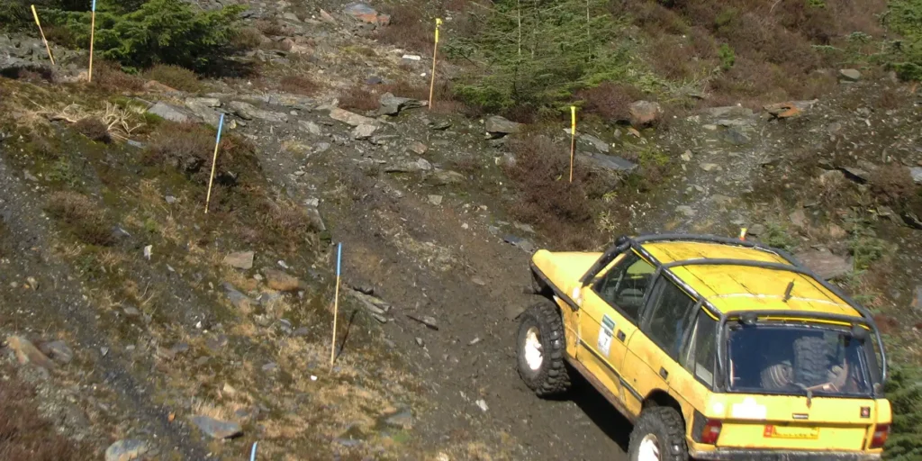 yellow range rover driving up a trials track.
